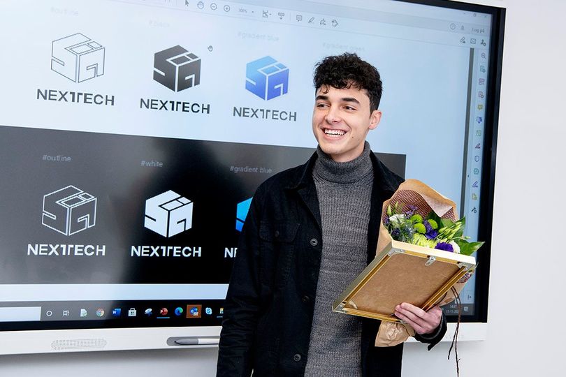 IBA Nexttech logovinder, Lorenze står foran skærm med logovarianter. Står med blomster og pris i hånden